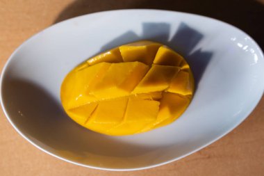 Kahverengi masanın üzerinde beyaz tabakta doğranmış mango.