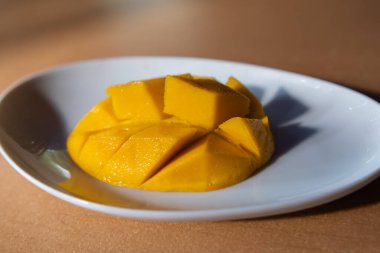 Kahverengi masanın üzerinde beyaz tabakta doğranmış mango.