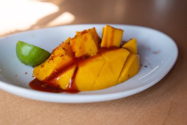 Plate of chopped mango with Mexican chamoy sauce and blurry background clipart