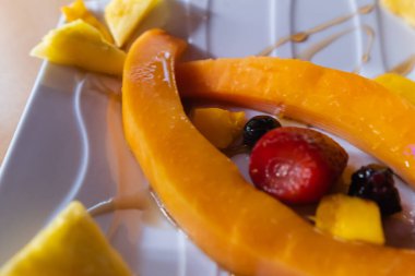 Taze meyve dilimleri ve kare porselen tabakta bal.