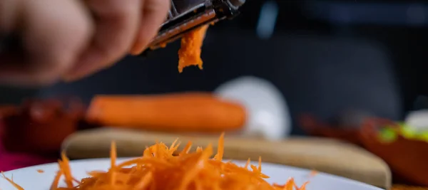 Hände schälen dünne Karotten mit Julienneschäler über weißem Teller — Stockfoto