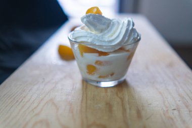 Tahta yüzeyde bir fincan şeftali, krema ve meyve dilimleri.