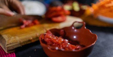 Arka planda daha fazla domates dilimleyen küçük kilden bir tencerede doğranmış domates.