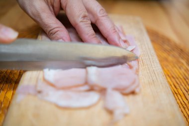 Kesme tahtasında taze hindi eti dilimleyen eller.