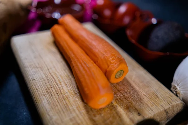 Loupaná mrkev na řezací desce obklopená více zeleninou — Stock fotografie