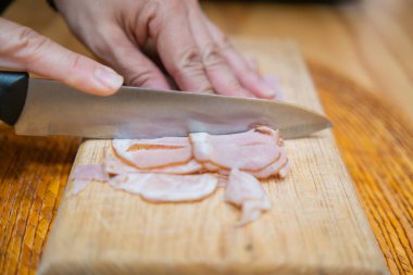 Kesme tahtasında taze hindi eti dilimleyen eller.