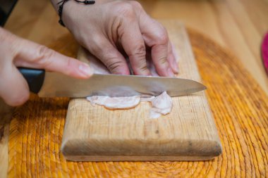 Kesme tahtasında taze hindi eti dilimleyen eller.