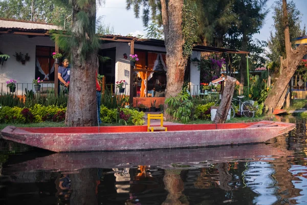 Arka planda bitkiler ve evler bulunan Xochimilco gölüne demirlemiş küçük bir tekne.