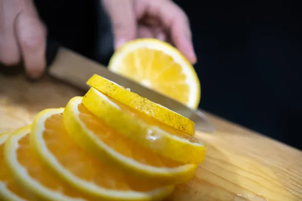 Hands slicing orange above wooden surface with black background — Stock Photo, Image