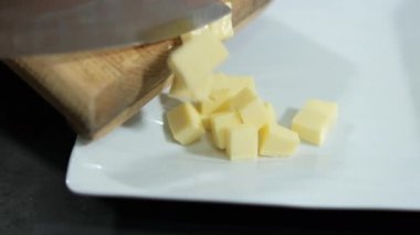 Bıçak, dilimlenmiş peyniri kesme tahtasından yavaşça süpürüyor.