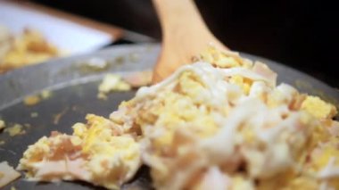 Spatula çırpılmış yumurta, doğranmış jambon ve erimiş Oaxaca peyniri topluyor.