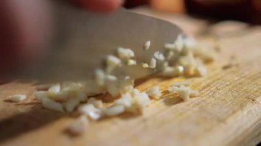 Tahta kesme tahtasının üzerinde sarımsak karanfili doğrayan eller.