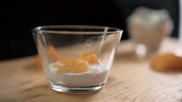 Fatias de pêssego caindo em copo de vidro com iogurte acima da superfície de madeira — Vídeo de Stock