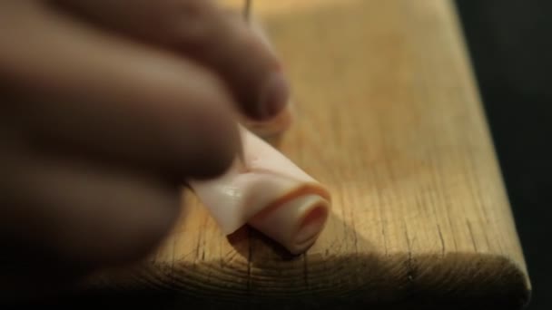 Manos insertando palillos en rollos de jamón de pavo por encima de la tabla de cortar — Vídeo de stock