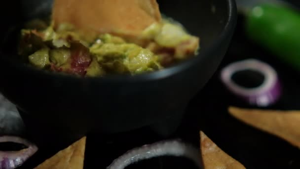 Mano mojar tortilla chip en un tazón de guacamole rodeado de chips de tortilla — Vídeos de Stock