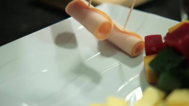 Hände legen Schinkenrollen auf einen Teller mit gewürfelter Fruchtpaste und Käsewürfeln — Stockvideo