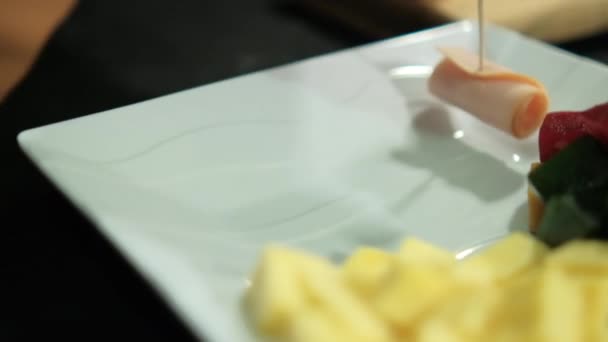 Manos colocando rollos de jamón en un plato con pasta de frutas cortadas en cubitos y cubos de queso — Vídeo de stock