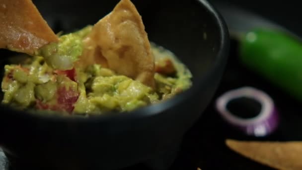 Chip tortilla ręcznie zanurzony w miseczce guacamole otoczony chipsami tortilla — Wideo stockowe