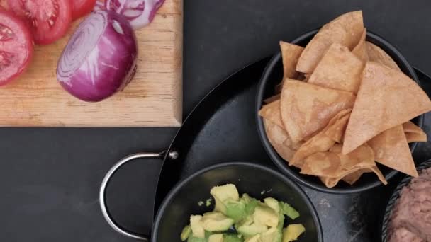 Verduras en rodajas y tazones de chips de tortilla y aguacate en la superficie negra — Vídeos de Stock