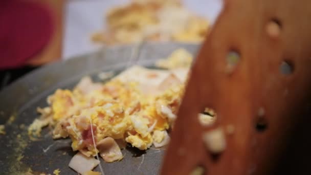 Drewniana szpatułka przewożąca jajecznicę z siekaną szynką indyka na okrągłym patelni — Wideo stockowe