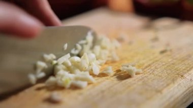 Tahta kesme tahtasının üzerinde sarımsak karanfili doğrayan eller.