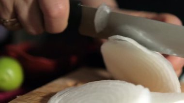 Tahta kesme tahtasının üzerinde soğan doğrayan eller.