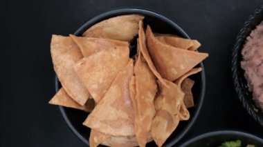 Siyah yüzeyde bir kase tortilla cipsi ve yeniden kızartılmış fasulye.