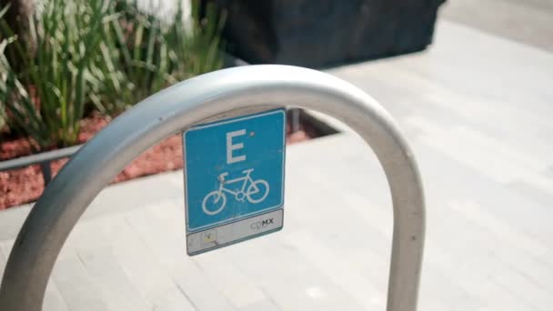 Señal de lugar de estacionamiento de bicicleta azul en arco de metal con tráfico como fondo — Vídeo de stock