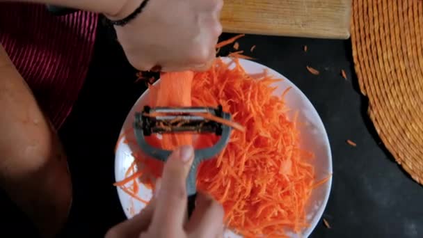 Hands peeling thin carrot with julienne peeler above white plate — Stock Video