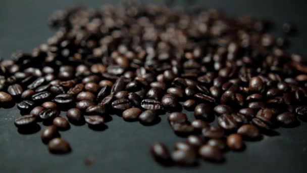 Bando de grãos de café torrados sendo derramados sobre a superfície preta — Vídeo de Stock