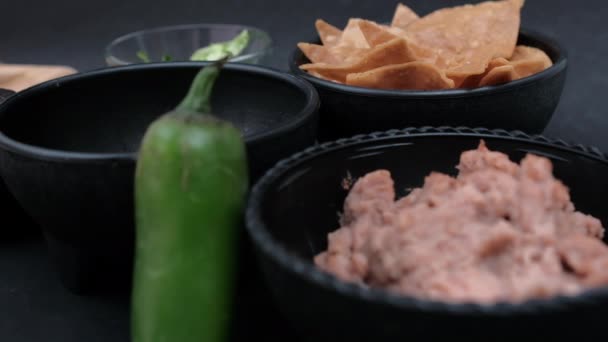 Chip de tortilla sumergido a mano en frijoles refritos en un tazón detrás de un chile — Vídeos de Stock