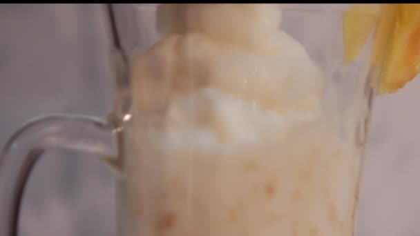 Häll vanilj milkshake i glas kopp med frukt på kanten — Stockvideo
