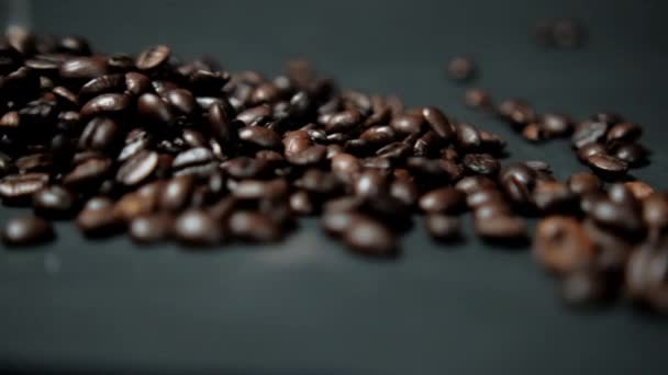 Жареные кофейные зерна выливаются из банки и попадают на черную поверхность — стоковое видео