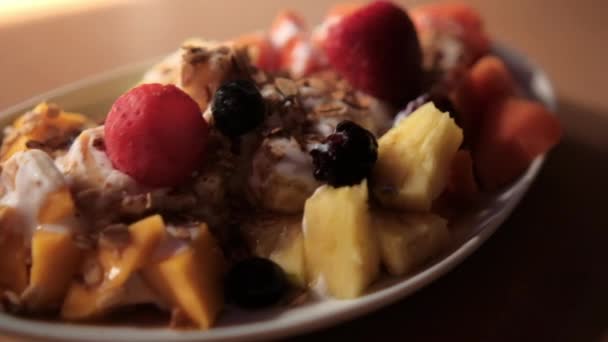 Тарелка нарезанных фруктов со сливками и овсянкой сверху — стоковое видео