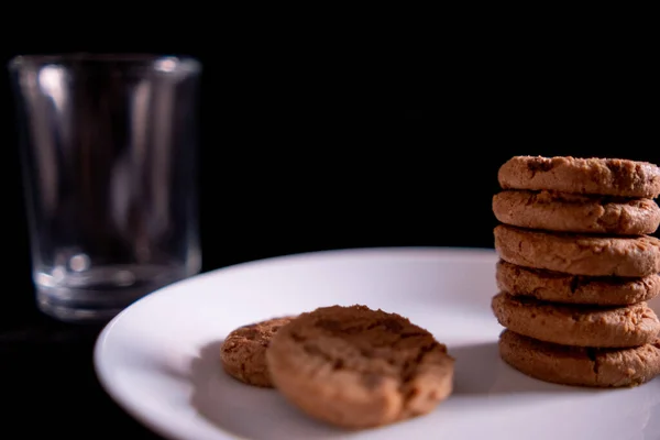 Galletas apiladas en plato blanco y vidrio vacío con fondo negro — Foto de Stock