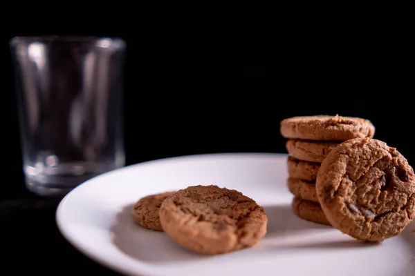 Galletas apiladas en plato blanco y vidrio vacío con fondo negro — Foto de Stock