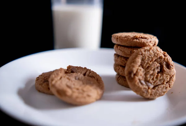 Stacked cookies on white plate and glass of milk with black background — Stock Photo, Image