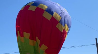 Mavi gökyüzünün altında renkli bir sıcak hava balonunu ısıtıp şişiriyor.