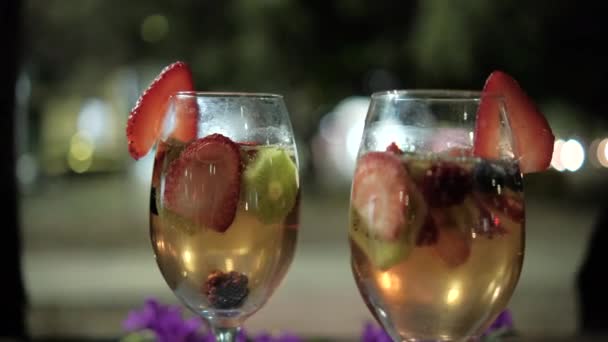 Dwie ręce brzęczące kieliszki do wina z plastrami owoców i ciemnym, rozmytym tłem — Wideo stockowe