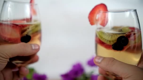 Két kéz csattogó borospoharak gyümölcsszeletek és fehér háttér — Stock videók