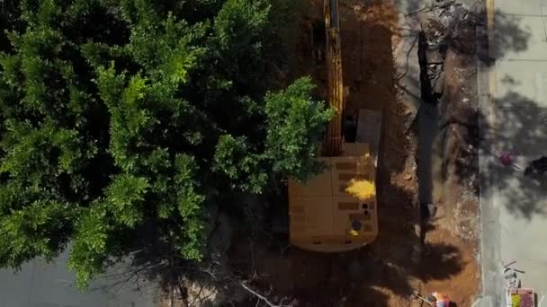 Vista aérea de uma escavadora escavando no canteiro de obras sob uma árvore — Vídeo de Stock