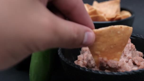 Mão mergulhando tortilla chip em feijão refrito em tigela atrás de uma pimenta — Vídeo de Stock