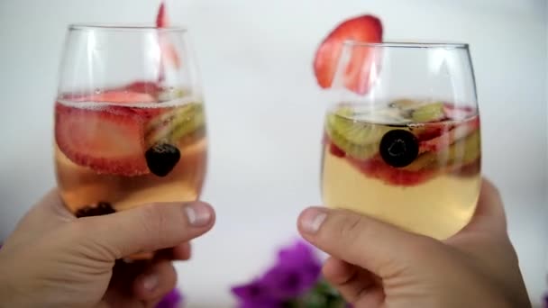 Dwie ręce brzęczące kieliszki do wina z plasterkami owoców i białym tłem — Wideo stockowe