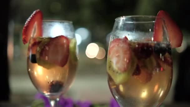 Meyve dilimli ve koyu bulanık arkaplanlı iki el şarap bardakları. — Stok video