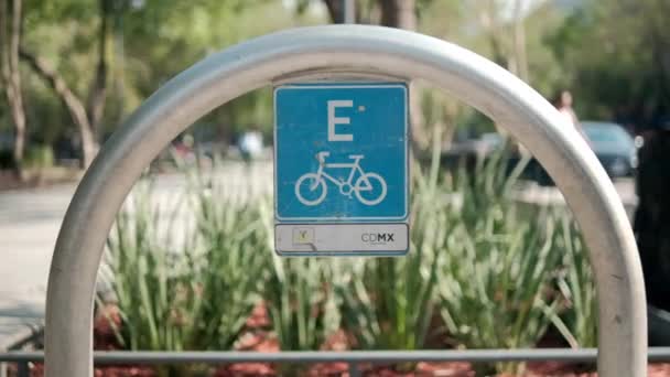 Arka planda ağaçlar olan metal kemerde mavi bisiklet park yeri işareti — Stok video