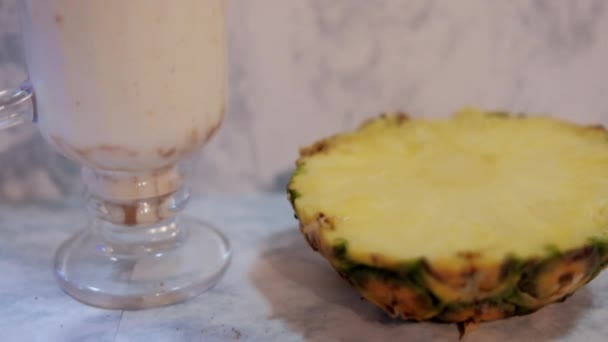 하얀 대리석 배경 위에 얹어 놓은 맛있는 바닐라 밀크 쉐이크와 파인애플 조각 — 비디오