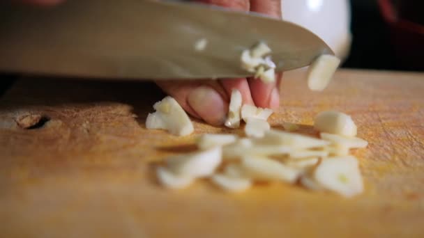 Handen snijden knoflookteentjes op een houten snijplank — Stockvideo
