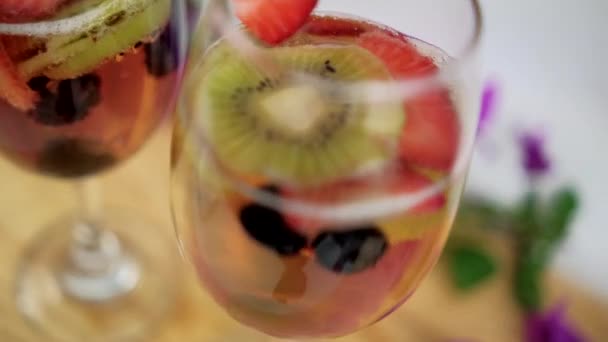 Drankjes met aardbeien en kiwi 's plakjes op houten ondergrond omgeven door bloemen — Stockvideo