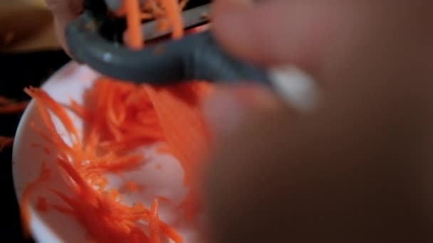 Manos pelando zanahoria fina con pelador de juliana sobre plato blanco — Vídeo de stock