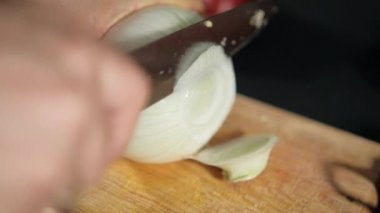Tahta kesme tahtasının üzerinde soğan doğrayan eller.